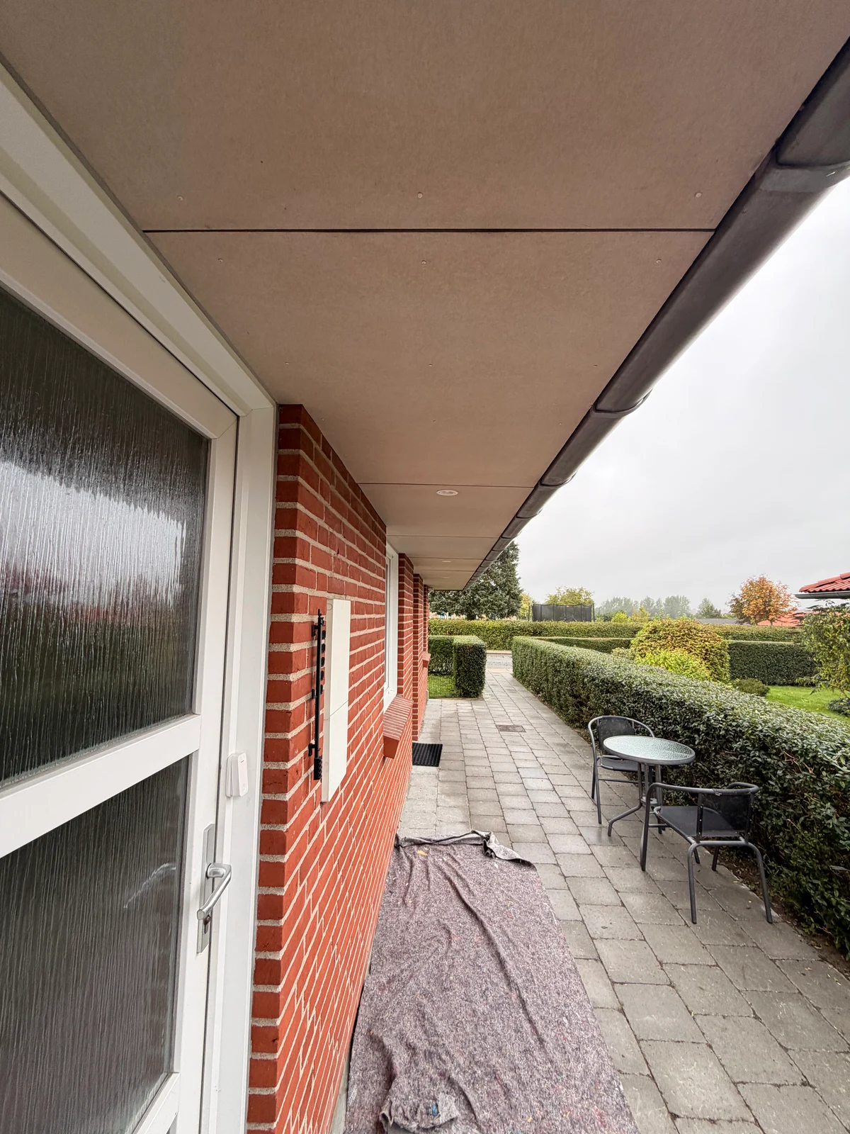 Ubehandlede plader under tagudhæng langs husets terrassedør før maling