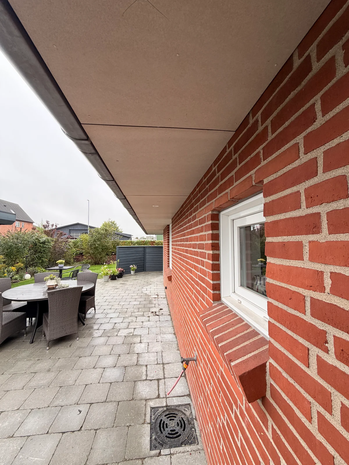 Tagudhæng med ubehandlede plader over et vindue i rød murstensfacade